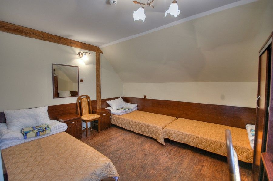 Attic-style triple bedroom with three single beds, wood-paneled headboard and warm lighting
