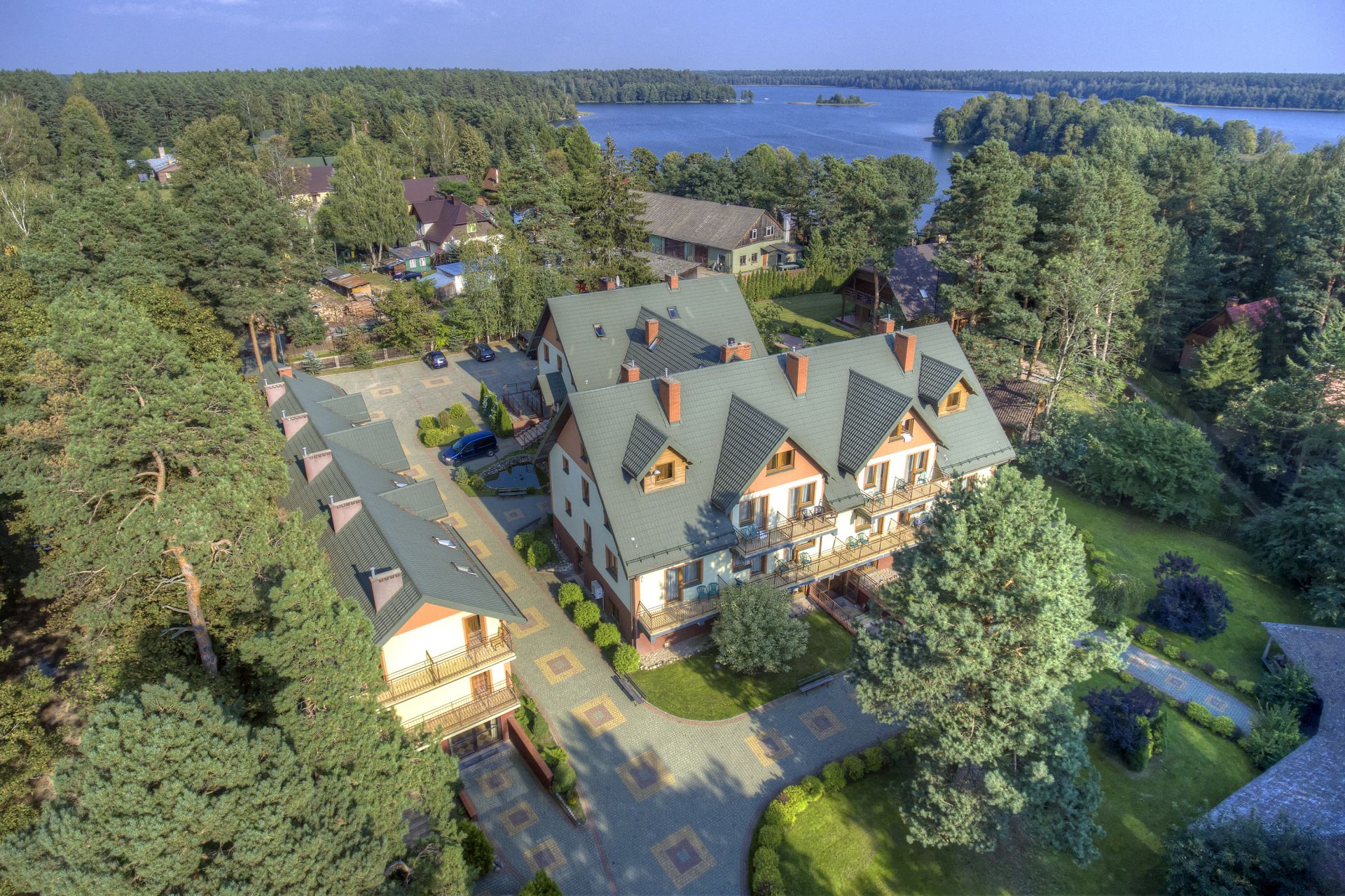 High-angle shot of resort complex with green-roofed buildings, winding paths and distant lake