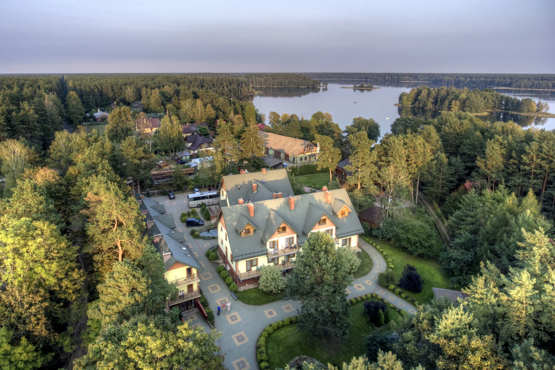 Aerial view of lakeside resort buildings nestled in dense pine forest by calm lake