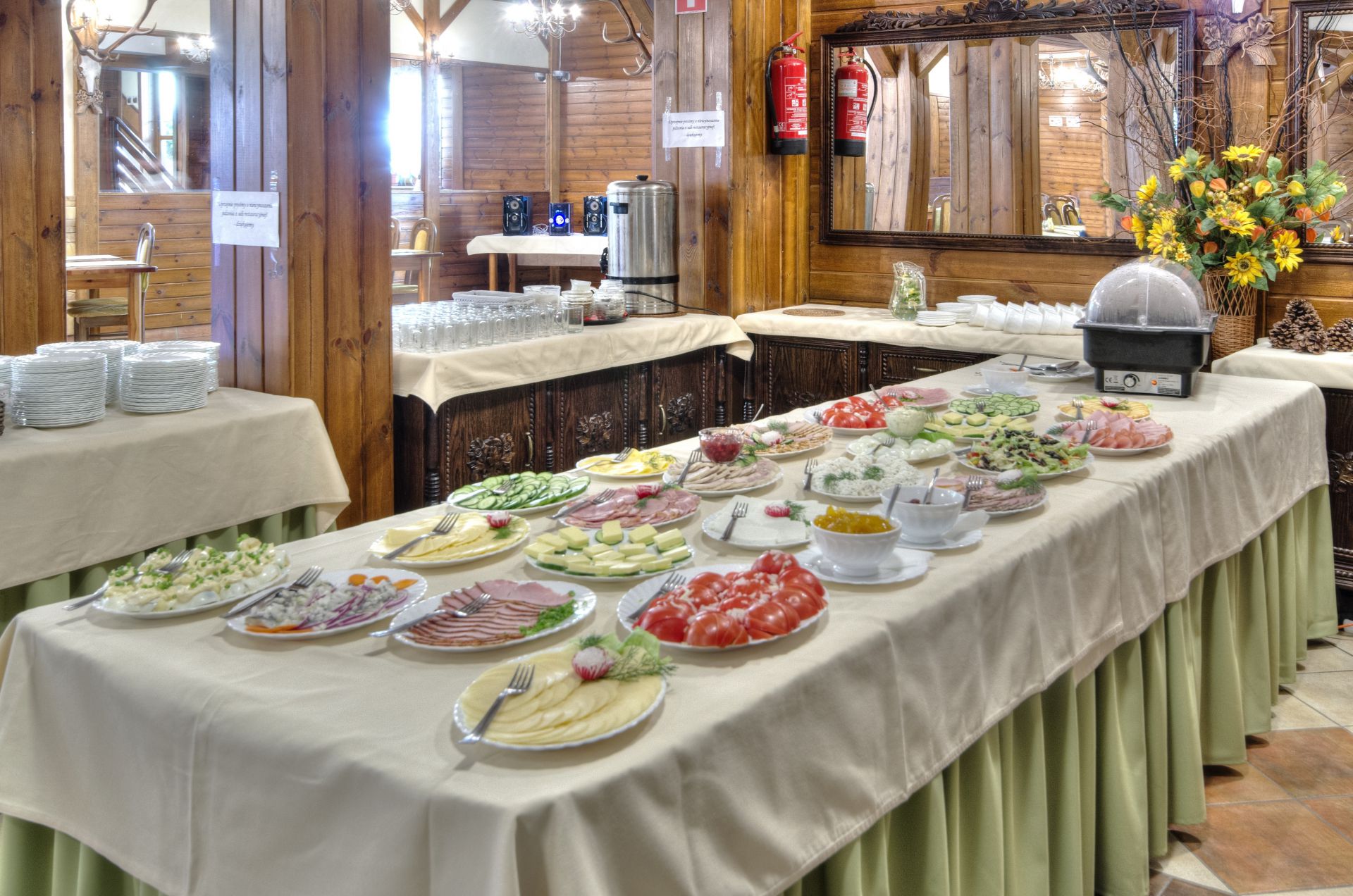 Buffet spread on linen-covered tables in rustic wooden dining room, assorted cold dishes and plates