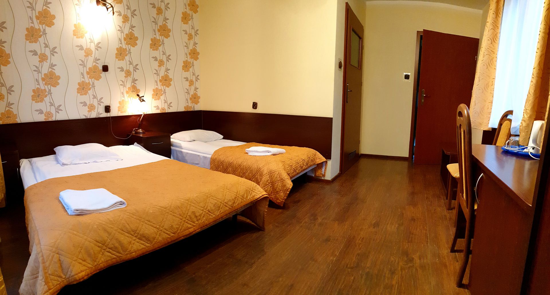 Hotel room with two single beds, orange bedspreads, bedside lamp and wooden desk.