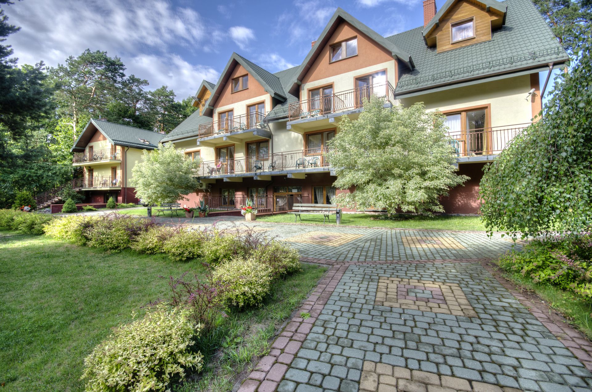 Three-story guesthouse with balconies, tiled roofs, paved courtyard and surrounding trees.