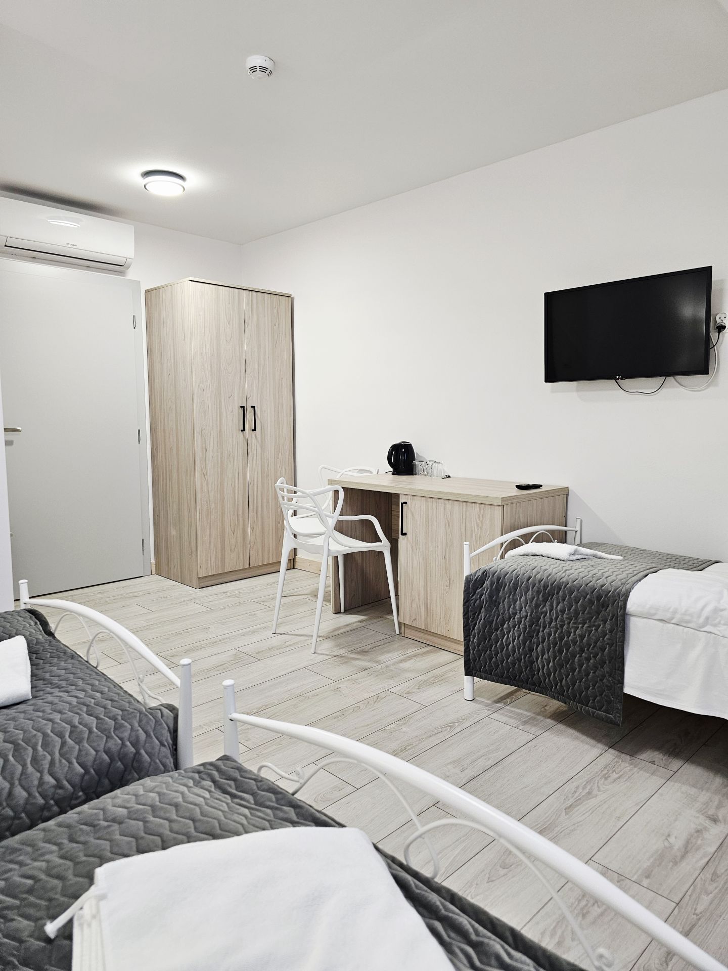 Twin beds with white metal frames, grey quilted throws and bedside wall lamps in minimalist room