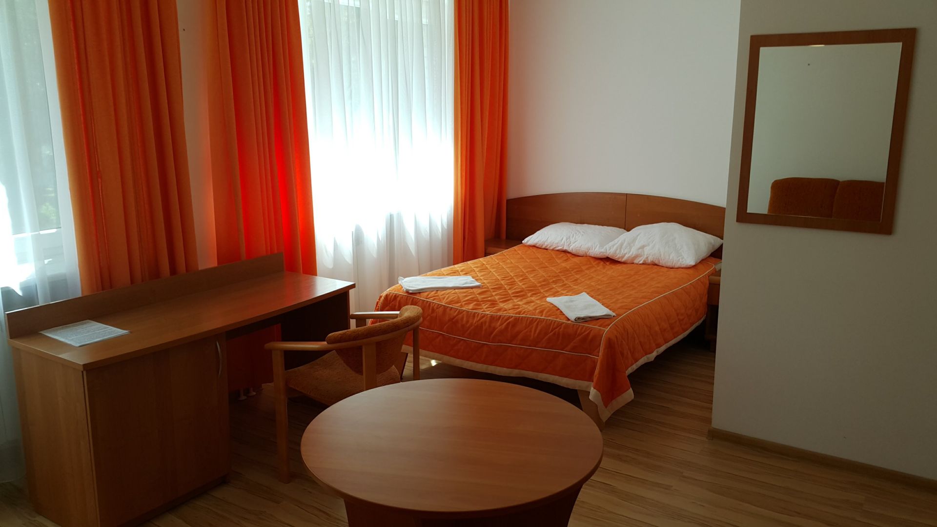 Spacious room with two single beds, small table, chairs and large window curtains.