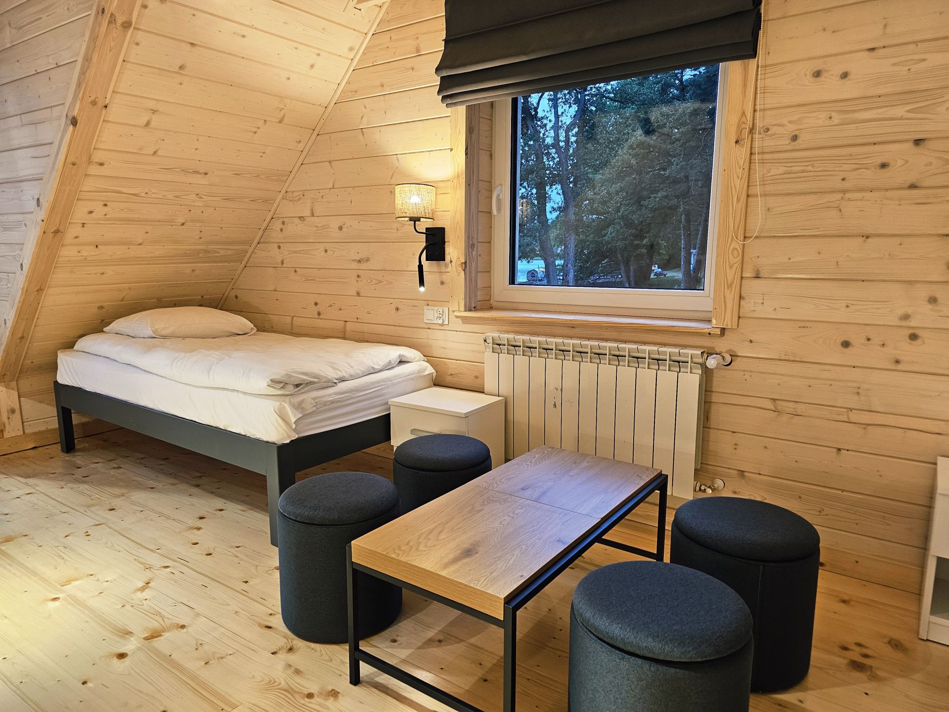 Slanted pine walls with window, bedside lamp, two neatly made single beds.
