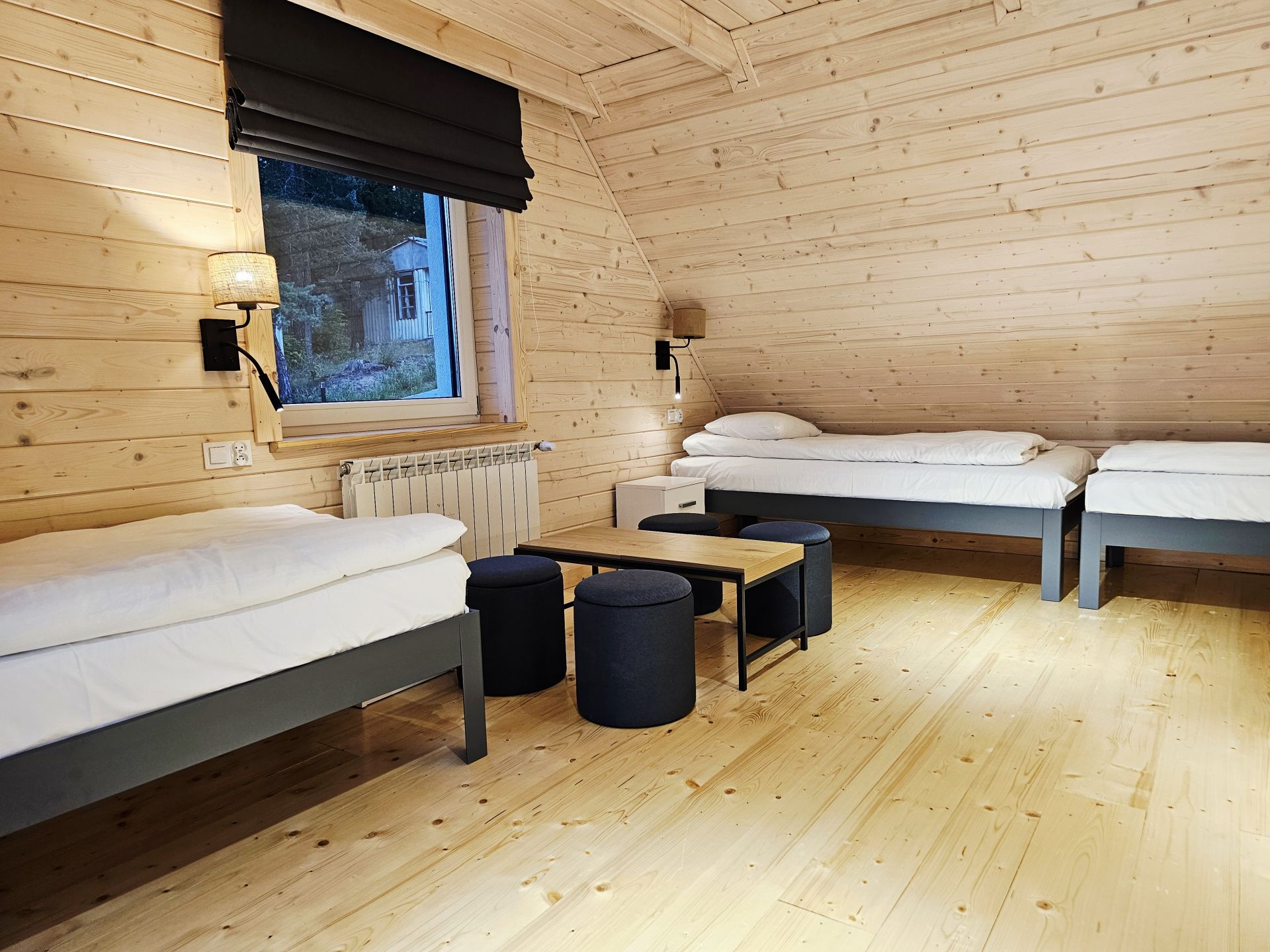 Angled wooden ceiling over twin beds, soft lamp lighting and small stools.