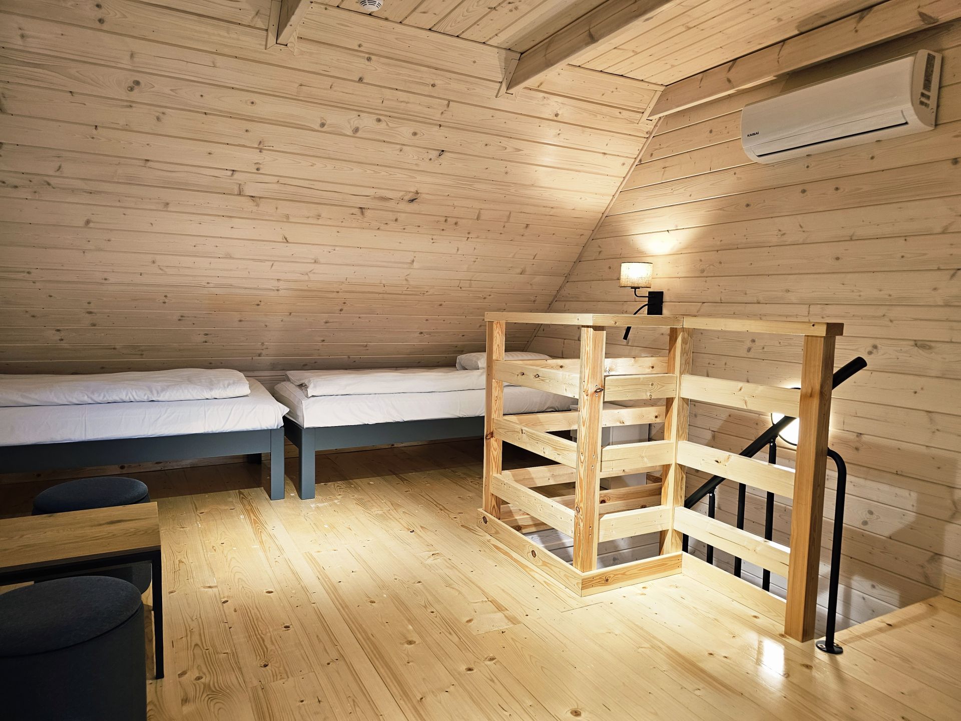 Cozy loft bedroom with two single beds, wooden walls and staircase railing.