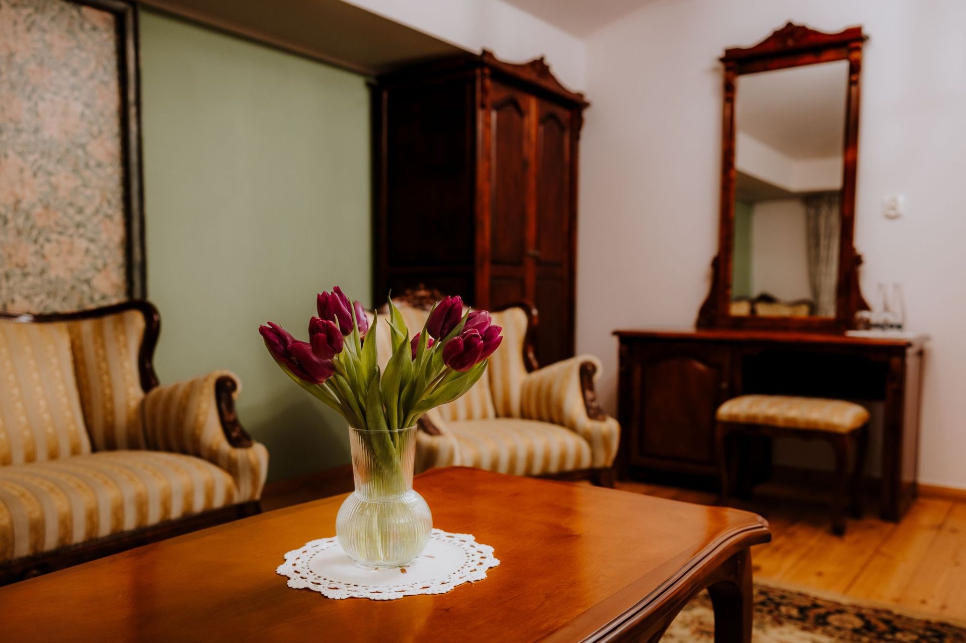 Purple tulips in glass vase on wooden table in cozy vintage sitting room with armchairs.