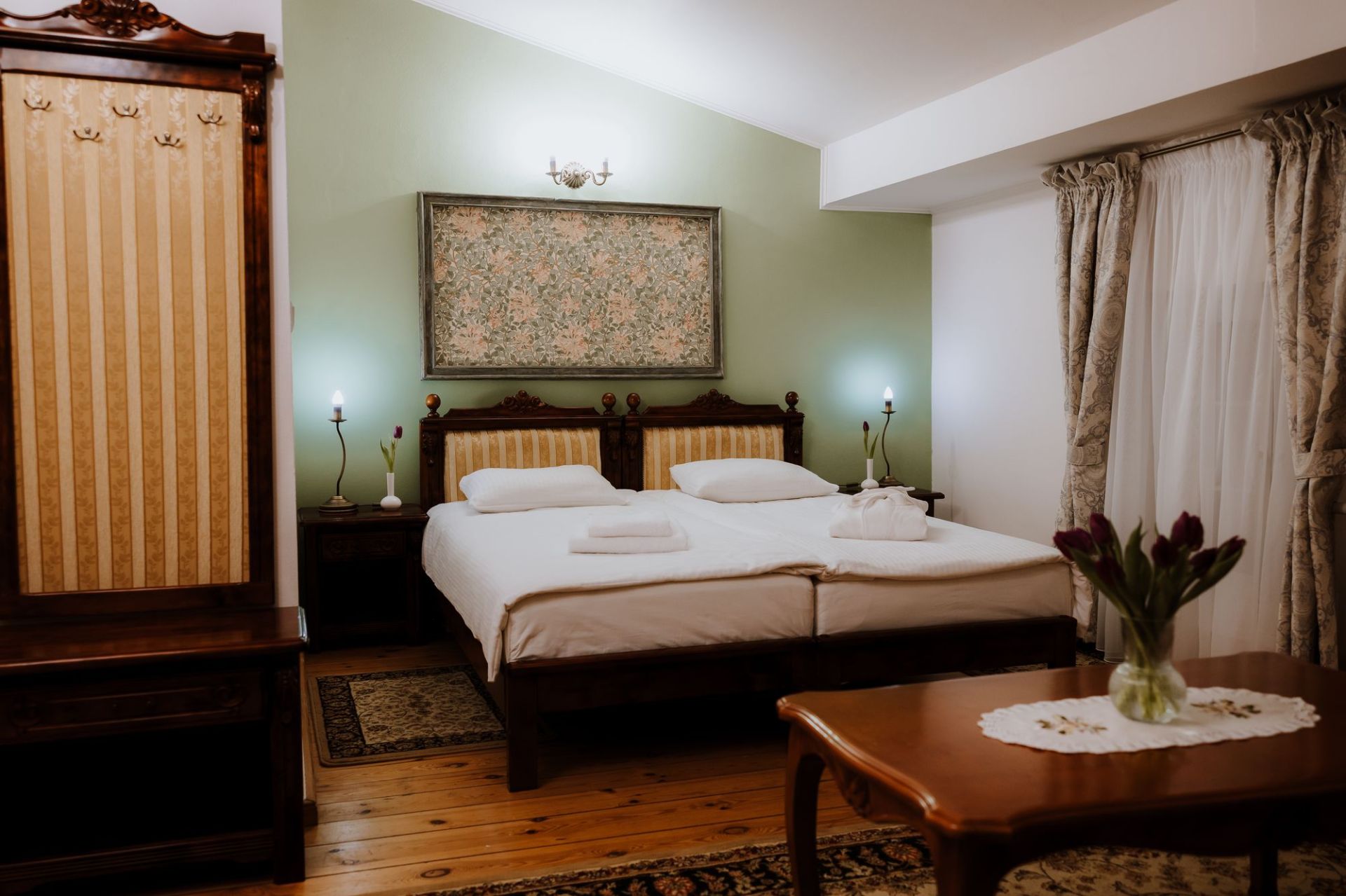 Twin beds with carved wooden headboard, bedside lamps and green accent wall creating a calm ambience.
